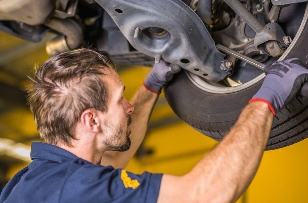 Mechanic inspecting the suspension and undercarriage of a vehicle at a tyre and mechanical workshop in Yandina