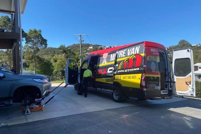 Mobile tyre service van changing a vehicle wheel onsite in a residential driveway.