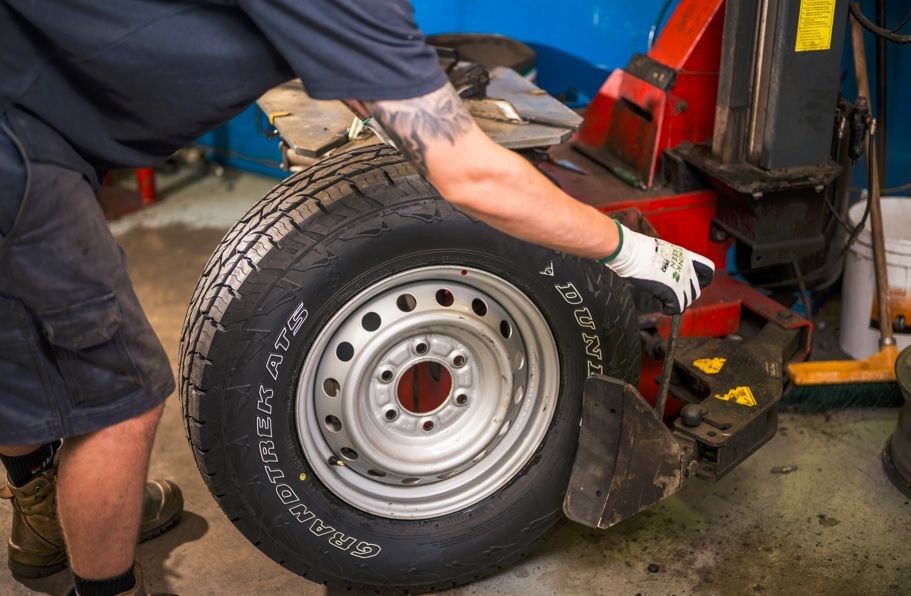 Mechanic fitting a Dunlop Grandtrek AT5 tyre onto a wheel in a tyre workshop.