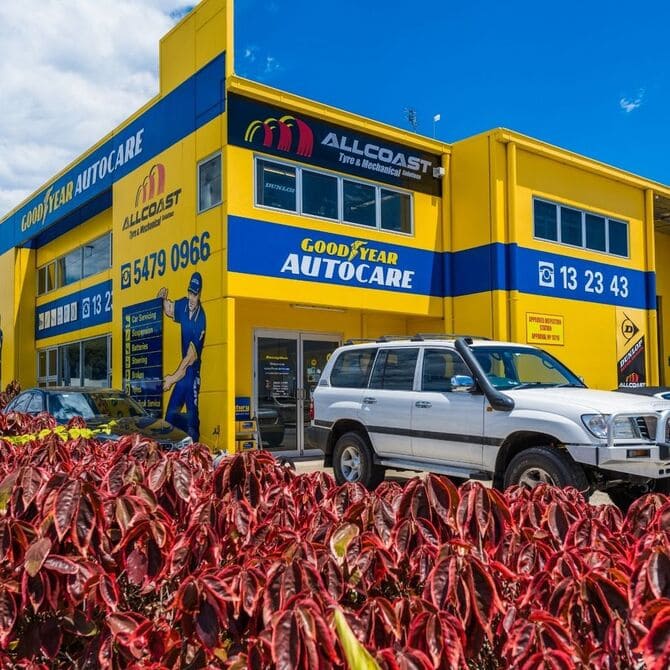 Front view of Allcoast Tyre & Mechanical Goodyear Autocare workshop with visible signage, vehicles, and red shrubs in foreground.