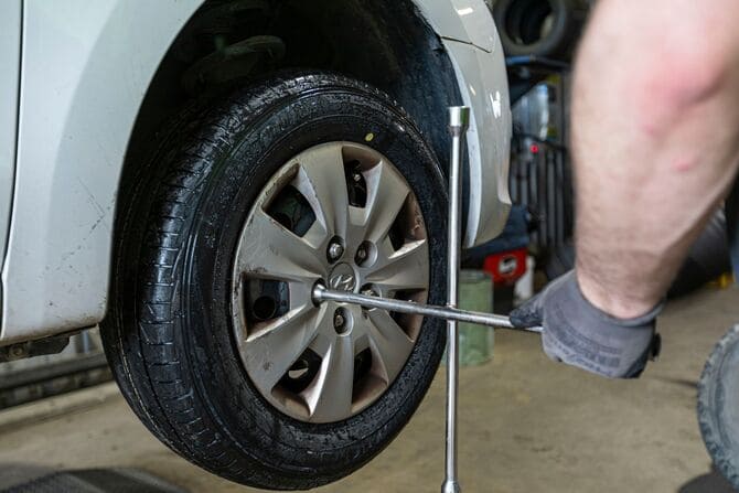 Mechanic tightening the lug nuts of a car wheel using a cross wrench while the vehicle is lifted